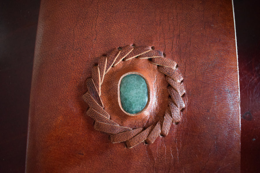 A leather-bound book of shadows with an aventurine crystal inlaid on the cover 