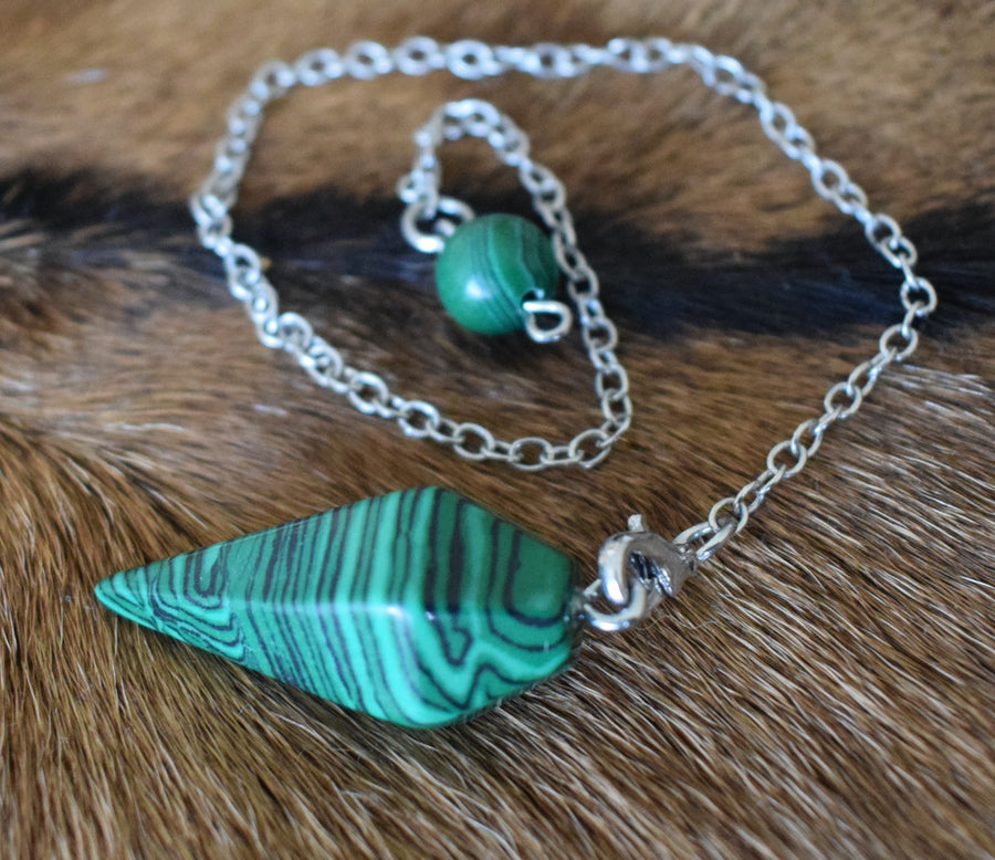 Mini malachite point crystal pendulum with chain and bead resting on goat skin fur
