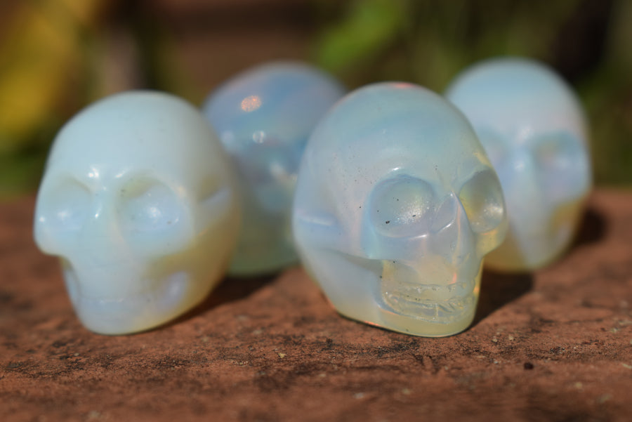 Four mini crystal opalite skulls resting on a rock.