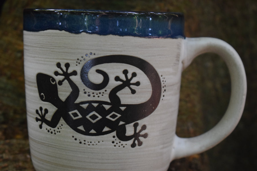A large cream mug with a blue rim and a lizard or gecko on the front.