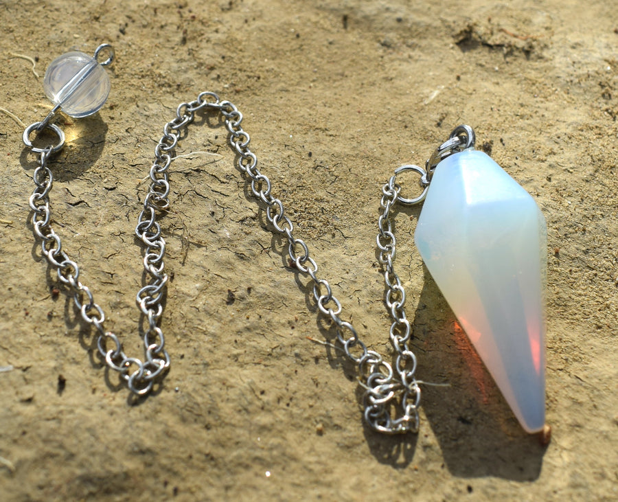 Small opalite point crystal pendulum with chain and bead resting on dry earth