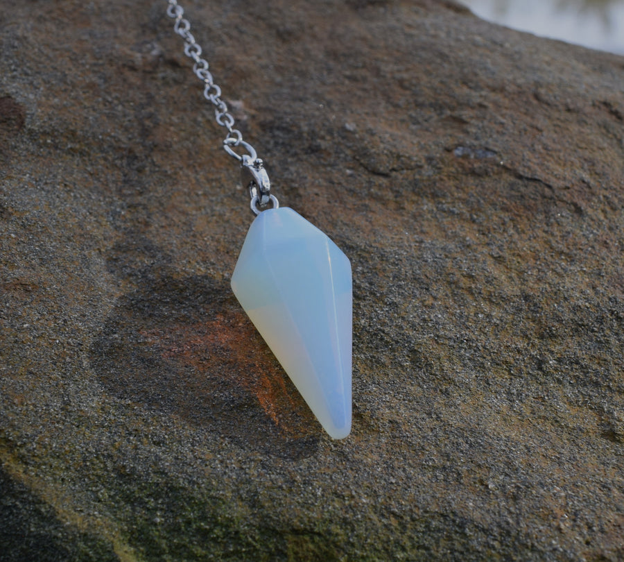 Small opalite point crystal pendulum with chain resting on rock