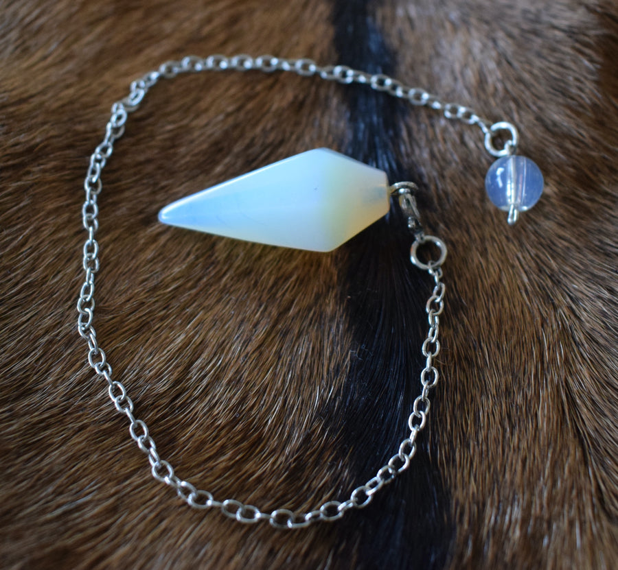 Small opalite point crystal pendulum with chain and bead resting on goat skin fur