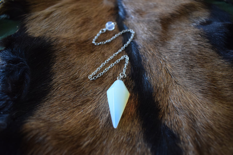 Small opalite point crystal pendulum with chain and bead resting on goat skin fur