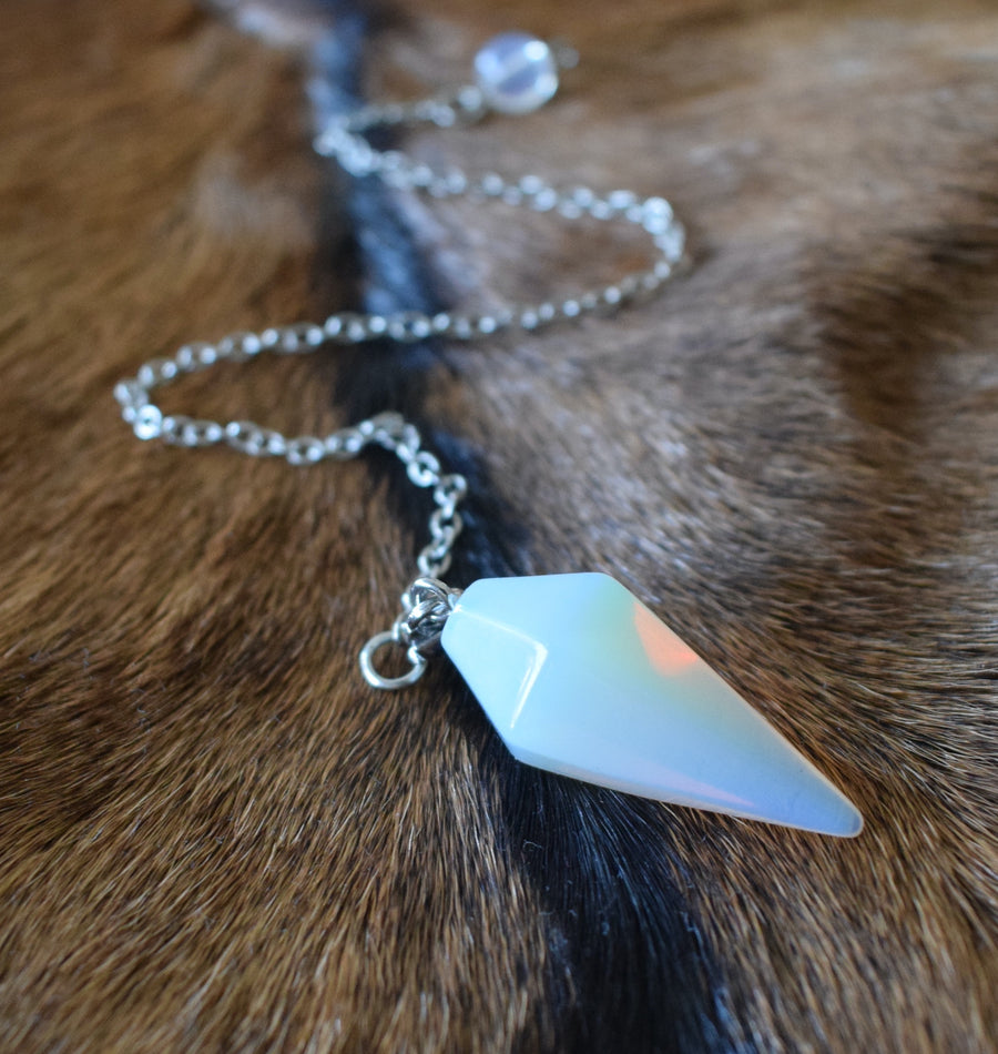 Small opalite point crystal pendulum with chain and bead resting on brown goatskin fur