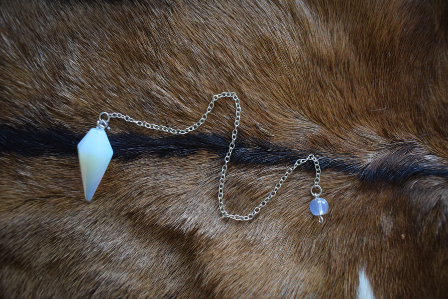 Small opalite point crystal pendulum with chain and bead resting on goatskin fur