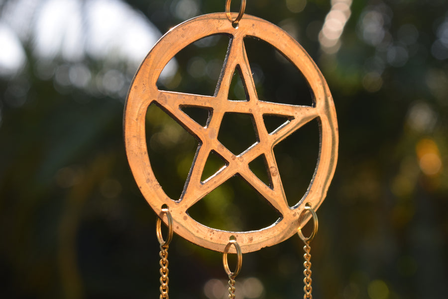 Bronze pentagram pentacle metal wind chime with background of mottled greenery in the garden