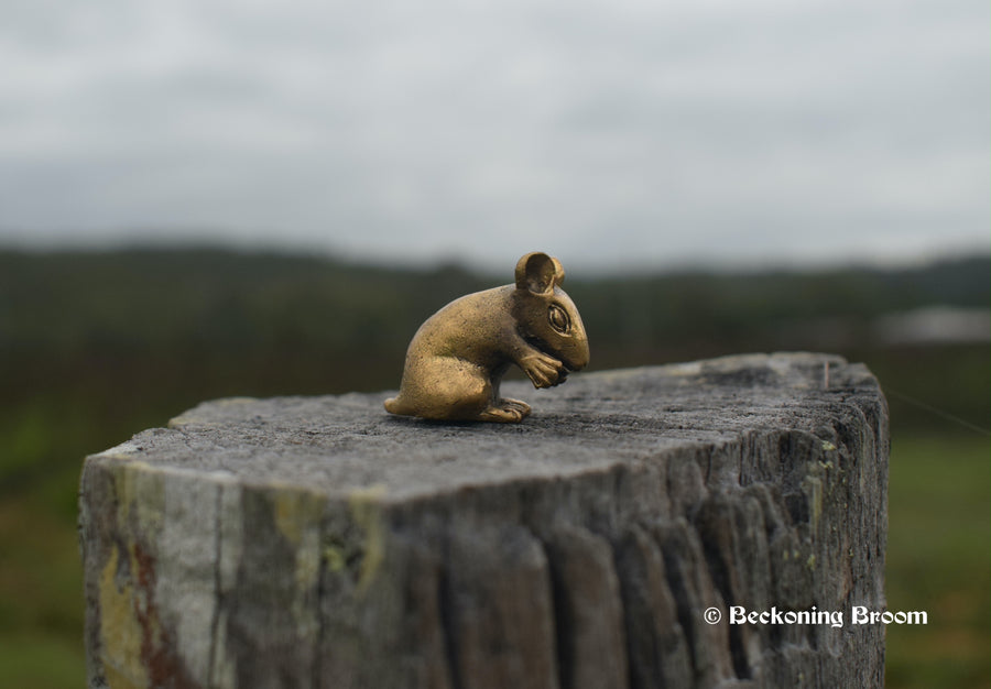 A miniature solid bronze statue of a rat resting on a old timber stump with mountains in the background