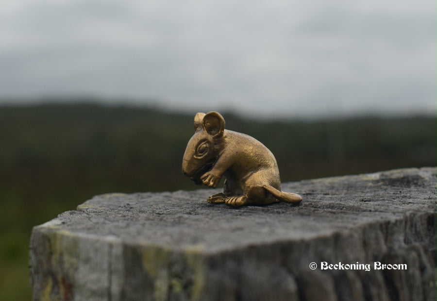A miniature solid bronze figurine of a rat resting on a old timber stump with mountains in the background