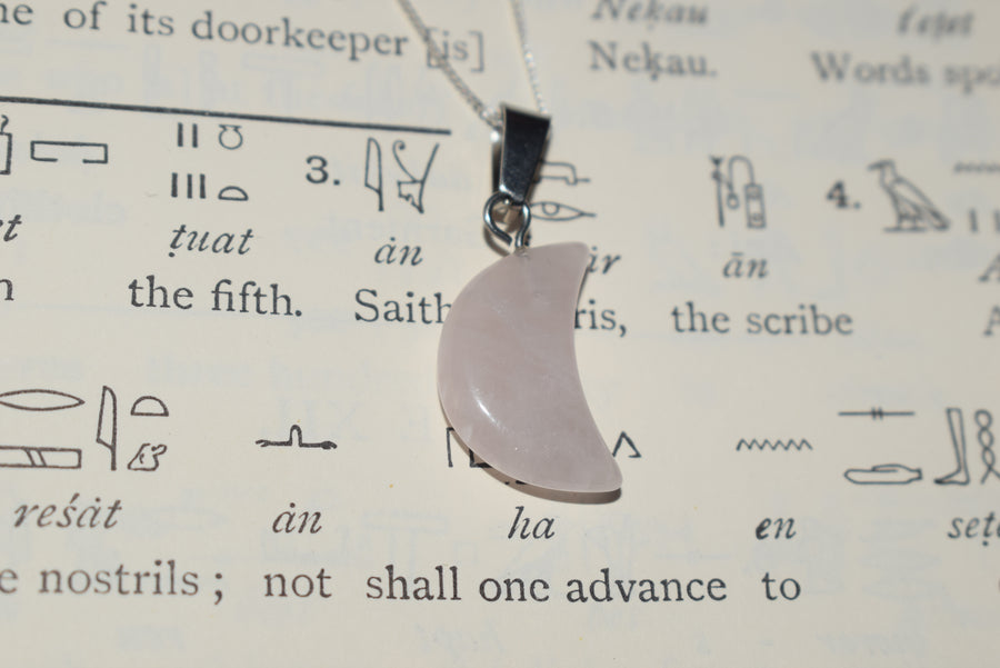 Rose quartz crescent moon pendant on silver chain resting on parchment of Egyptian hieroglyphics