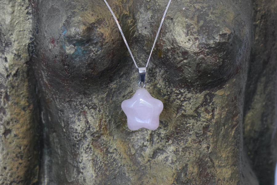 A rose quartz crystal pentagram star necklace on a sterling silver chain hanging on the neck of a bronze goddess sculpture