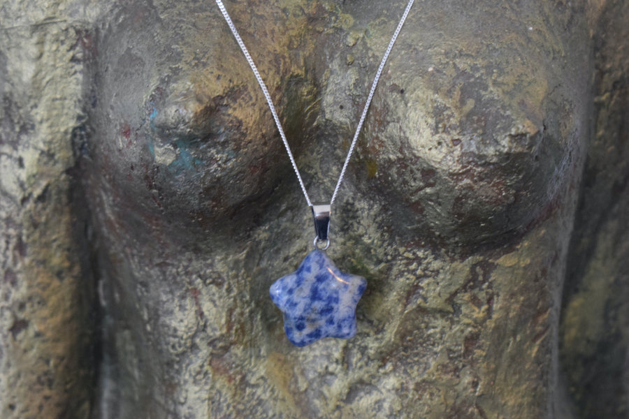 A sodalite crystal crescent moon necklace on a sterling silver chain hanging on the neck of a bronze goddess sculpture
