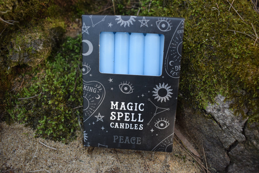 A pack of 12 light blue tapered candles with Magic Spell Candles and Peace written on the pack, rests on a bed of moss.