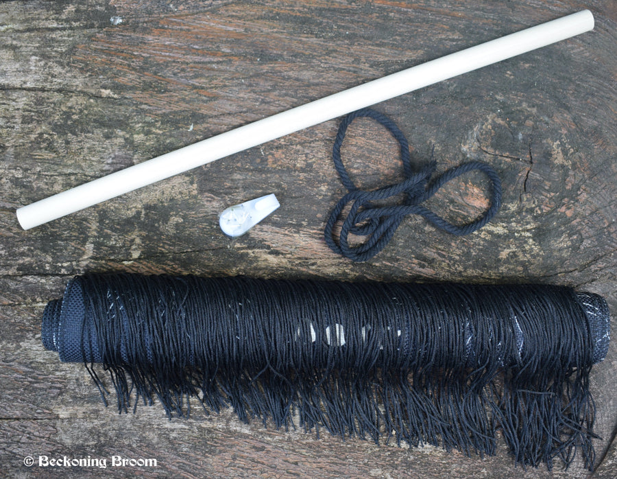 A rolled up black fabric tapestry with a piece of dowel, rope and hook rests on a piece of wood.