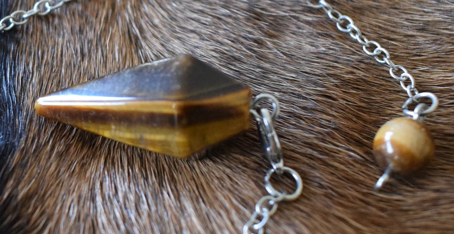 Mini Tiger's Eye point crystal pendulum with chain and bead resting on goatskin fur