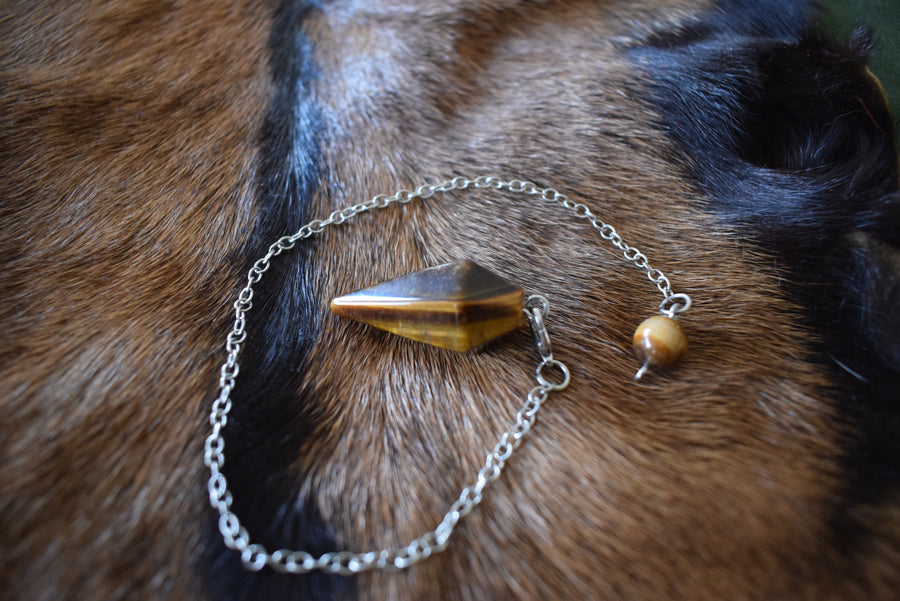Small Tiger's Eye point crystal pendulum with chain and bead resting on brown goatskin fur