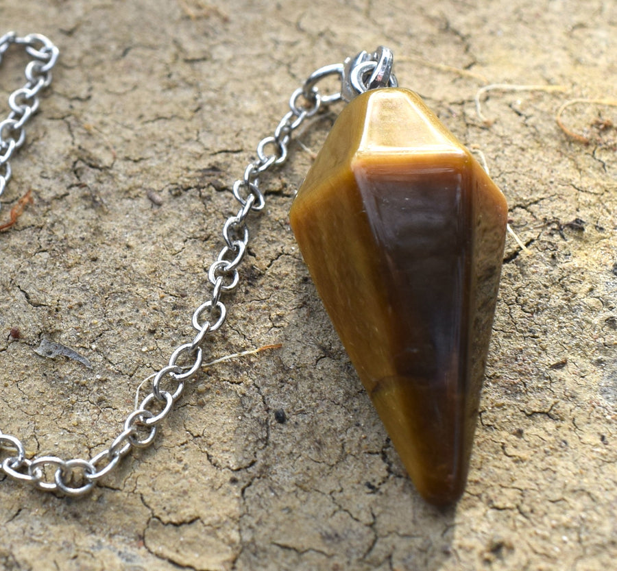 Mini Tiger's Eye point crystal pendulum with chain resting on cracked dry earth