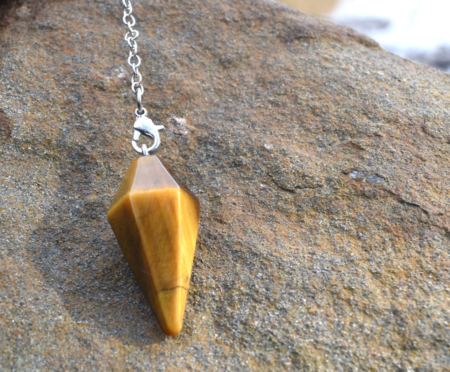 Mini Tiger's Eye point crystal pendulum with chain hanging on rock