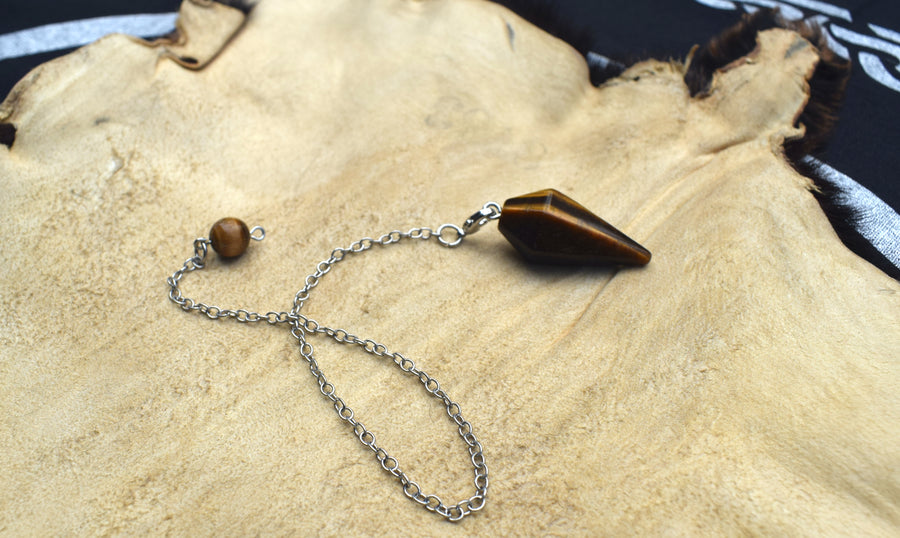 Mini Tiger's Eye point crystal pendulum with chain and bead resting on animal skin