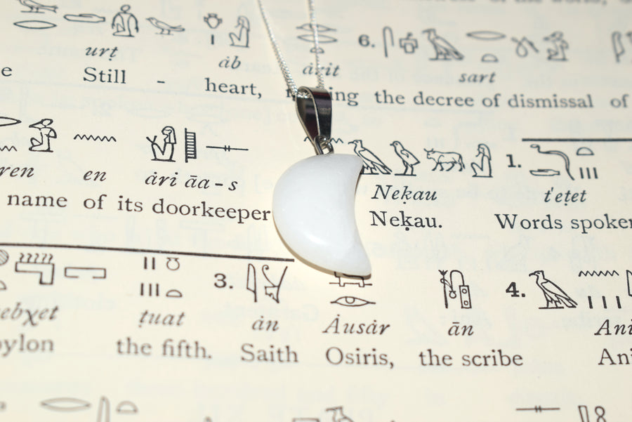 White quartz crescent moon pendant on sterling silver chain resting on Egyptian hieroglyph parchment