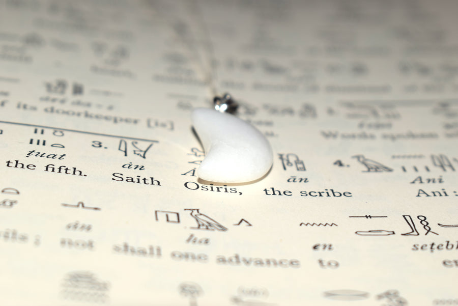 White quartz crescent moon pendant on sterling silver chain resting on Egyptian hieroglyphic parchment