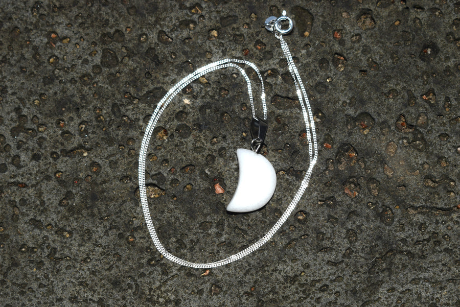 White quartz crescent moon pendant on sterling silver chain circled around it with rock background