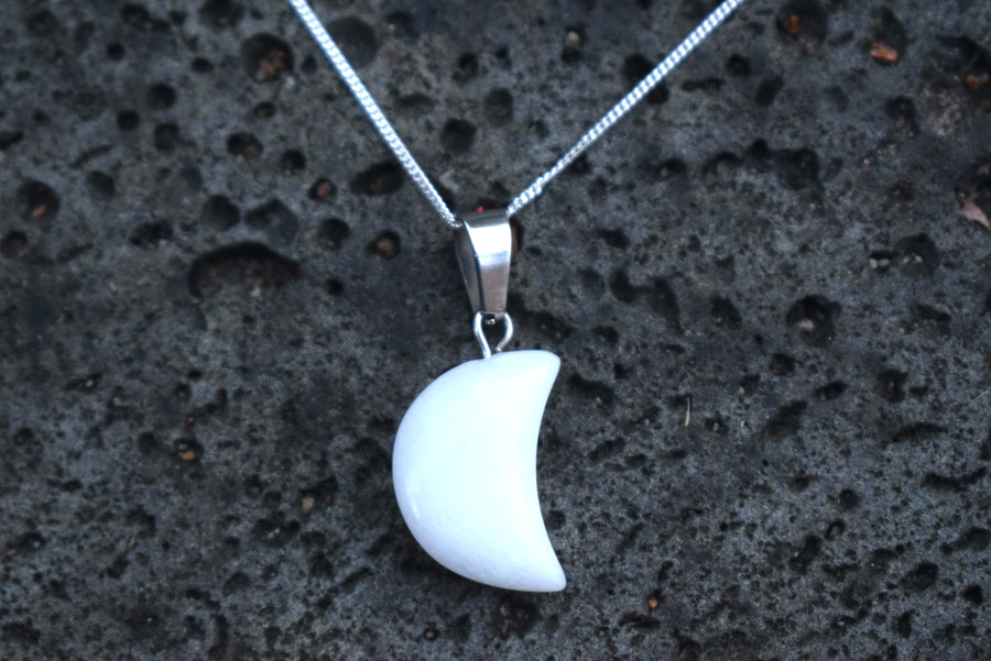 White quartz crescent moon pendant on sterling silver chain resting on rock