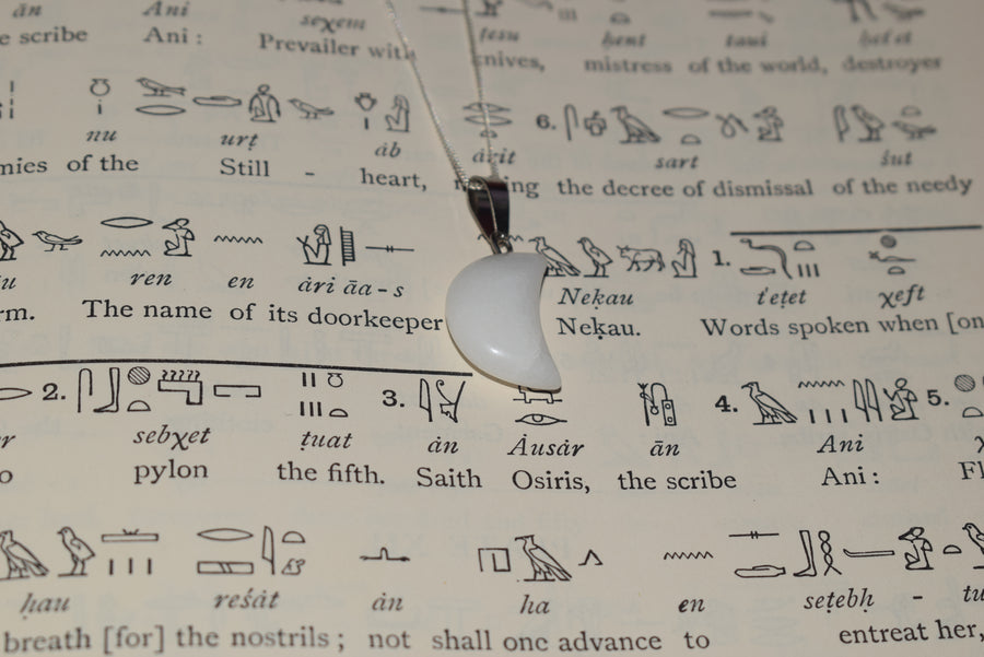 White quartz crescent moon pendant on sterling silver chain resting on Egyptian hieroglyph parchment