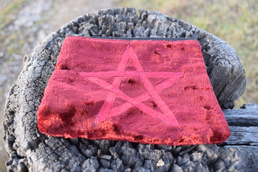 Red velvet zippered bag with pentagram on the front resting on weathered timber paling