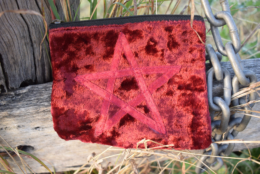 Red velvet zippered bag with pentagram on the front resting on weathered timber paling with old chain