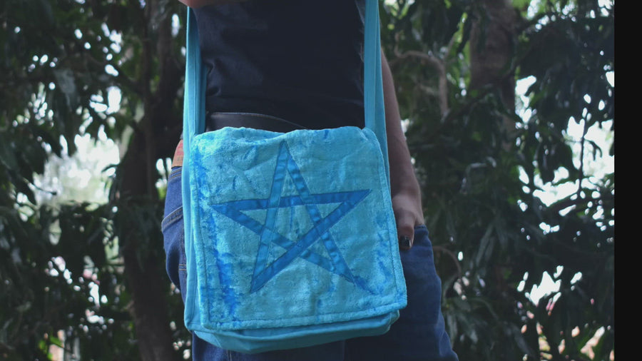 Person taking book out of a light blue shoulder bag with pentagram on the front