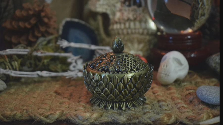 A video of metal lotus trinket box filled with white sand with a lid resting on a wooden pentagram trivet nestled on a bed of autumn leaves