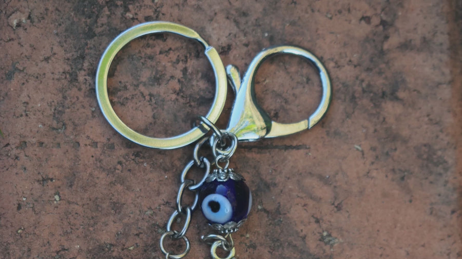 Two key rings with two evil eye beads and two silver coloured leafy trees rests on paperbark bark.